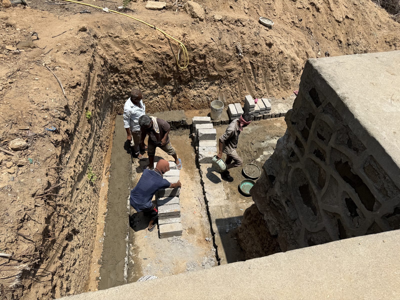 Workers laying concrete block masonry inside an excavated percolation chamber
